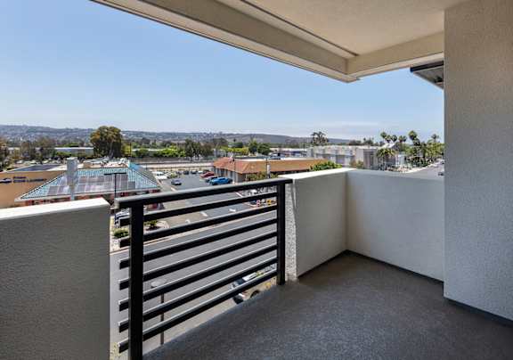 A balcony with a black railing overlooks a parking lot and buildings.