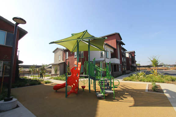 A playground with a green umbrella and a red slide.
