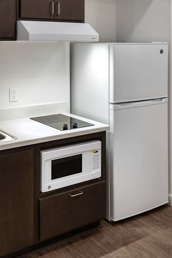A white refrigerator stands next to a microwave in a kitchen.