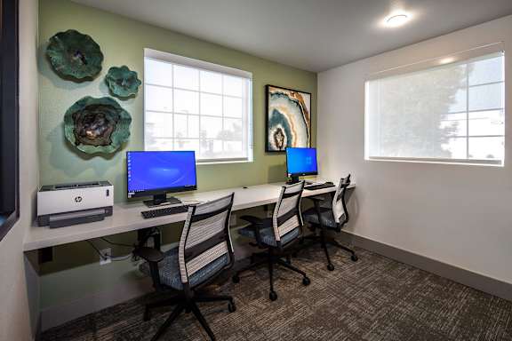 A room with a desk, chairs, and two monitors.