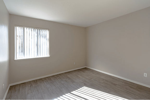 an empty bedroom with a window and wooden floors