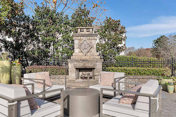 A fireplace is in the middle of a patio with white chairs around it. at Echo at Lake Norman, Mooresville, NC