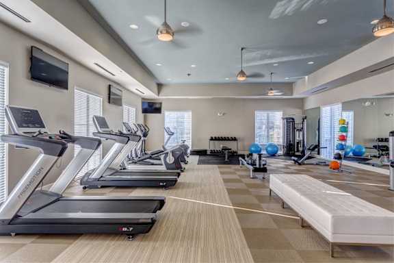 a gym with cardio machines and a television on the wall