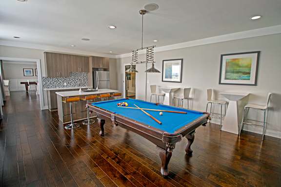 A pool table in a room with wood flooring and a bar area.