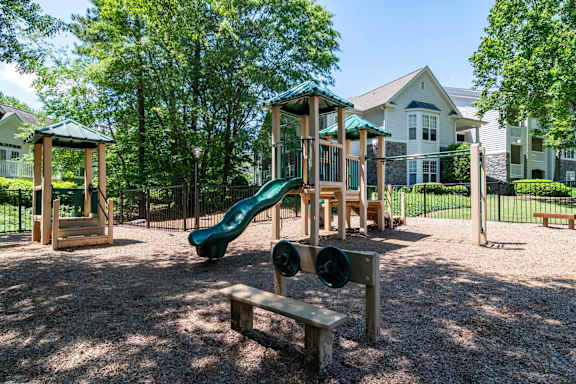 A playground with a green slide and a wooden bench.