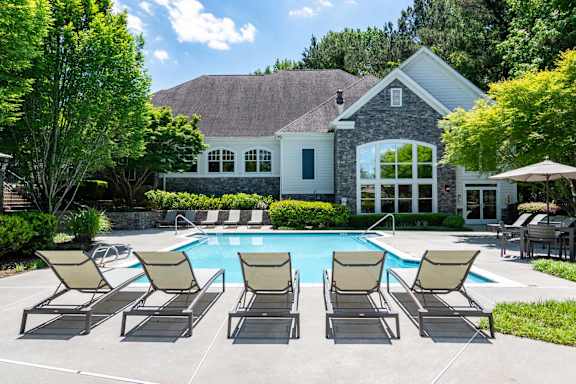 A pool surrounded by chairs and a house in the background.