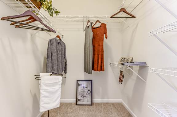 A white closet with clothes hanging and a picture frame on the floor.