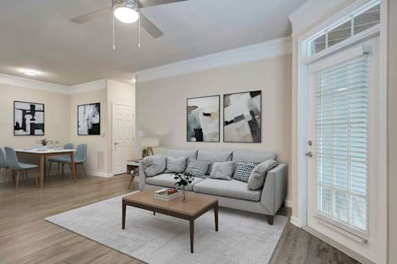 A living room with a grey couch, a dining table with chairs, a coffee table, and pictures on the wall.