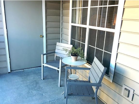 A small table with a plant on it sits between two chairs on a porch.