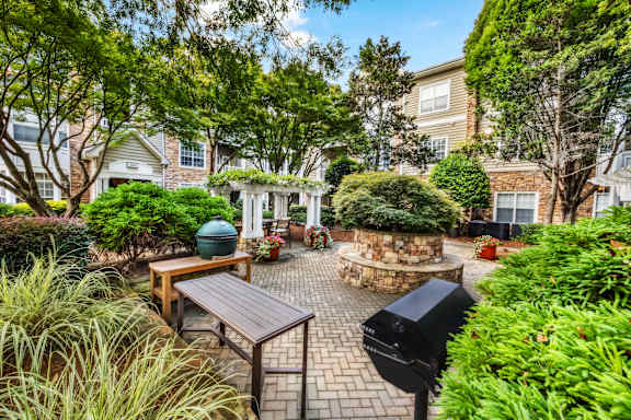 A backyard with a bench, a fire pit, and a tree.