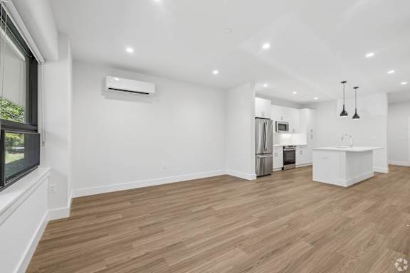A spacious room with wooden flooring and a kitchen area in the background.