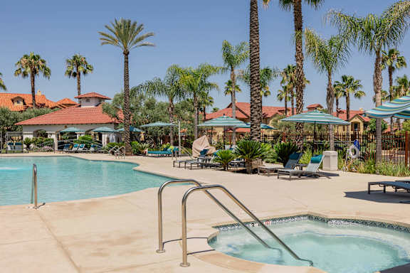 A pool surrounded by palm trees and a few buildings.