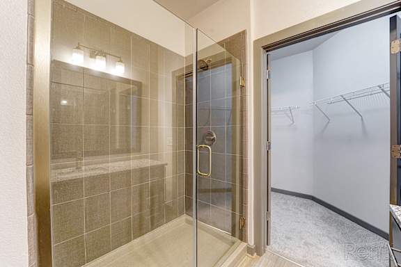 A bathroom with a glass shower stall and a glass door leading to a laundry room.