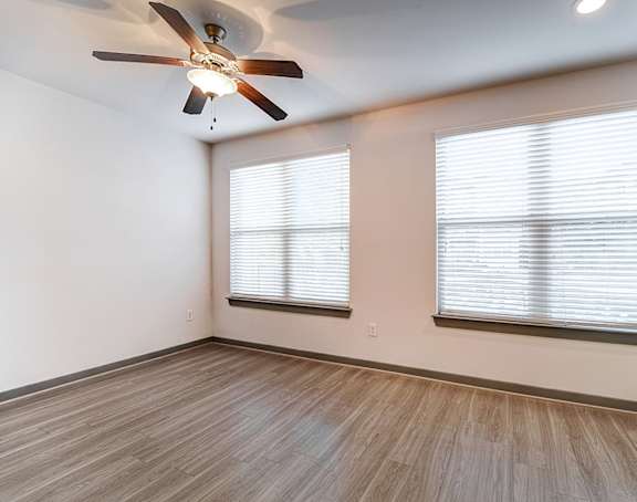 A room with a ceiling fan and two windows with blinds.