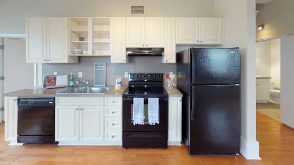 A black refrigerator stands in a kitchen with white cabinets.