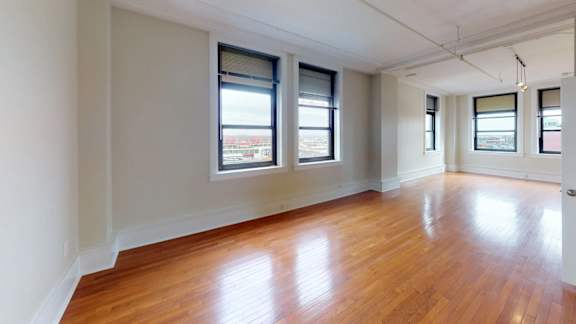 A room with wooden floors and three windows.