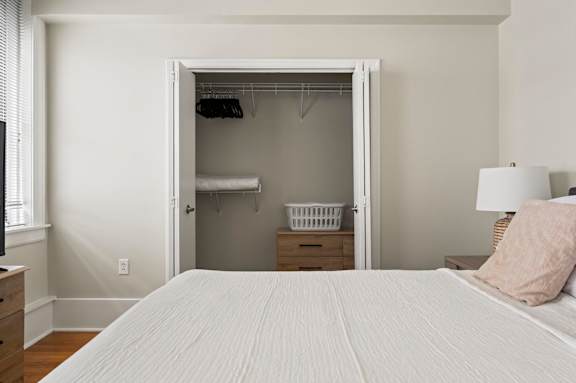 A bedroom with a large bed and a closet with clothes hanging.
