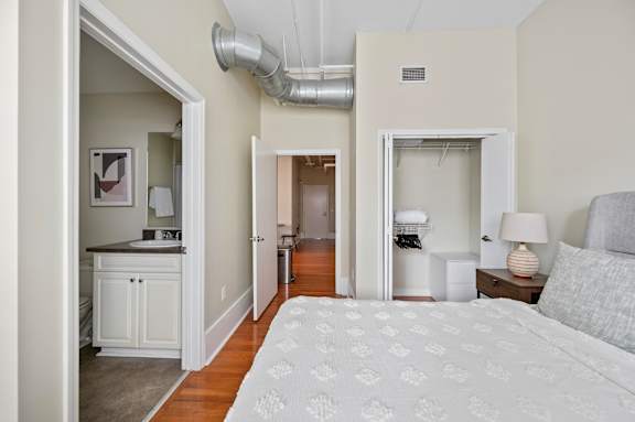 A bedroom with a bed, nightstand, and a small kitchen area.