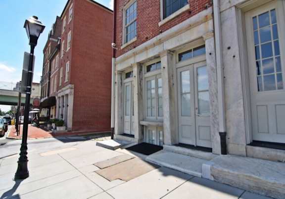 A street view of a building with a red brick wall and white trim.