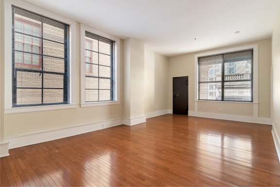 A room with wooden floors and three windows.