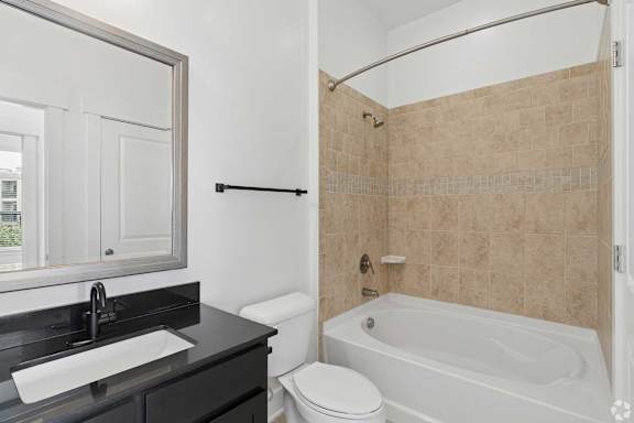 A bathroom with a white toilet, a black sink, and a beige tiled shower.