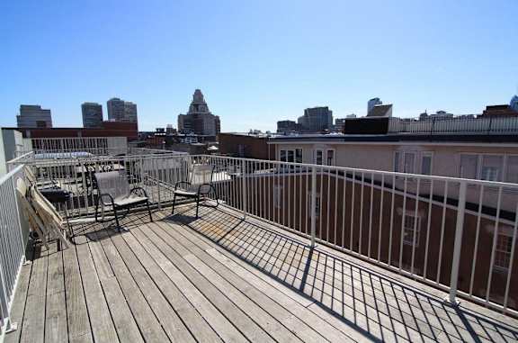 A wooden deck with a metal railing and chairs overlooking a city skyline.