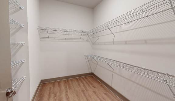A walk-in closet with wooden floors and metal wire shelving.