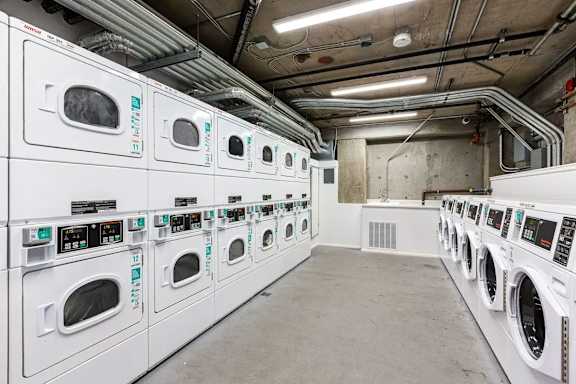 A row of white front loading washing machines in a laundromat.