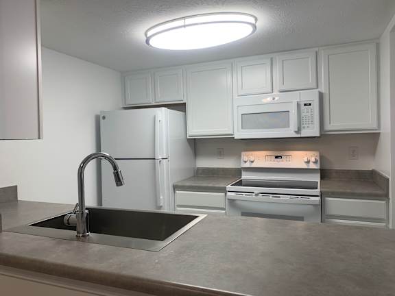 A kitchen with a sink, refrigerator, microwave, and oven.