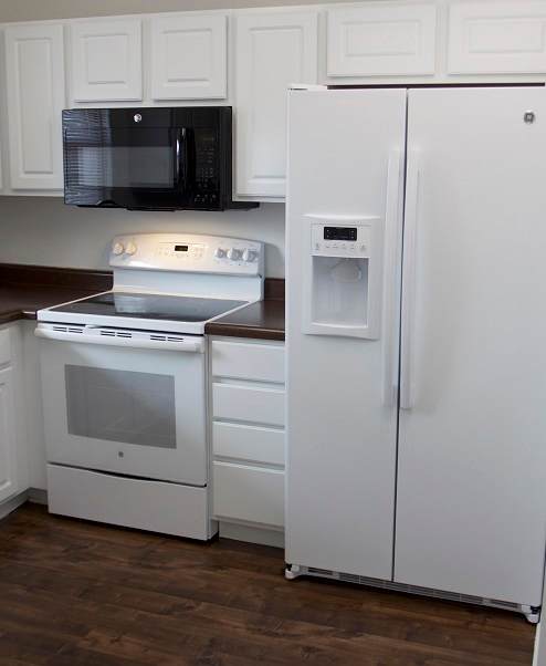 A white refrigerator stands in a kitchen next to a microwave and oven.