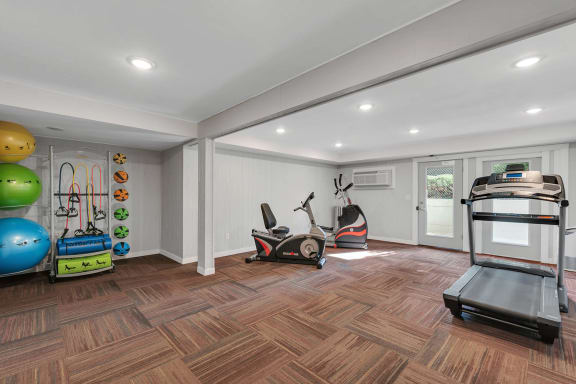 Fitness center with elliptical, sitting bike, treadmill, medicine balls, yoga balls, resistance balls and windows on the back wall.