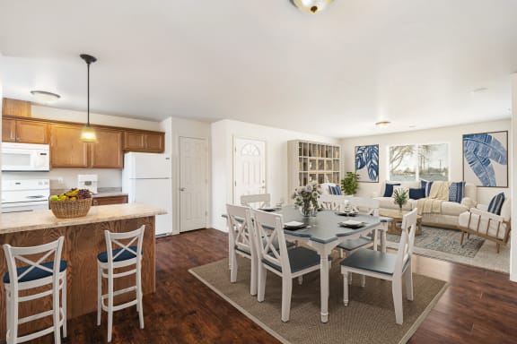 Kitchen opens up to the dining area and living room. Staged with dining set, couch, two chairs, wall bookshelf, and rugs. at Pine Tree Park, Washington