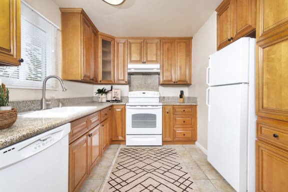 Apartment Kitchen with granite counters, white appliances including a dishwasher, stove/oven and fridge. Ample cabinet space at Pacific Sands, San Diego, CA