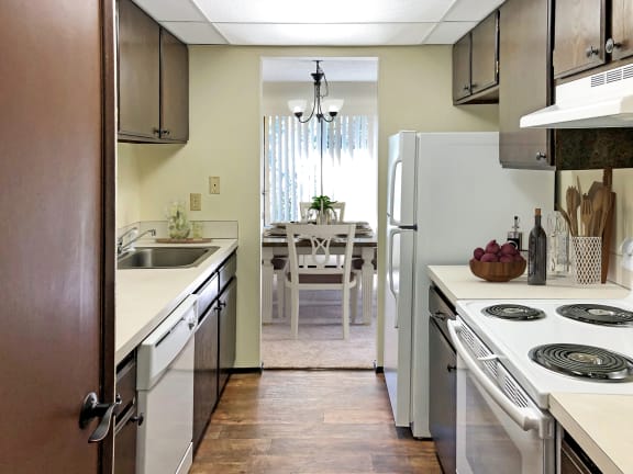 a galley-style kitchen with white appliances, top and bottom cabinets and a view to the dining room.