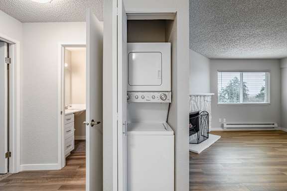 A white fridge in a kitchen with a door open leading to washer and dryer at Peak 88 Apartments in Renton, WA..