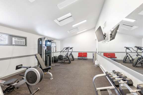 A gym with a variety of equipment including a rowing machine, dumbbells, and a bench.