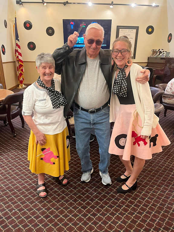 Three people are standing in a room with a flag in the background.