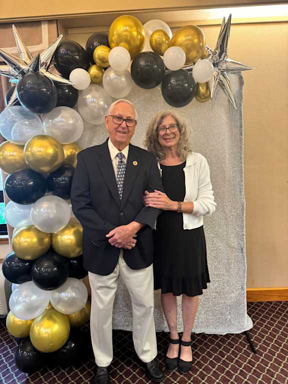 A man and woman stand in front of a balloon arch.