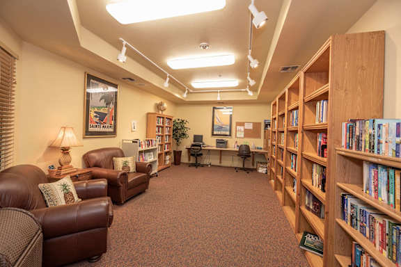 a library with furniture and shelves of books  at Winding Commons Senior Living, Carmichael, CA