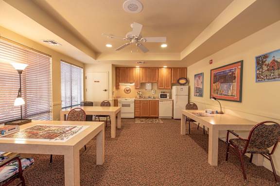 a dining room with tables and chairs and a kitchen with a ceiling fan  at Winding Commons Senior Living, Carmichael, CA, 95608