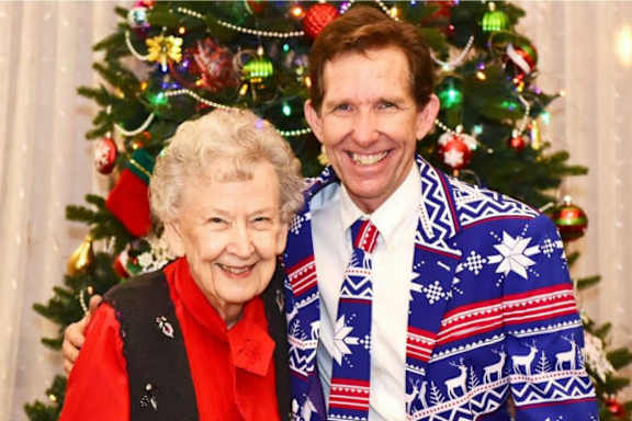 a man and a woman wearing ugly sweaters in front of a christmas tree