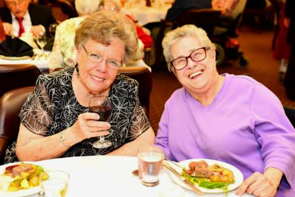 two women sitting at a table with food and a glass of wine