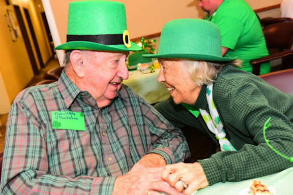 an old man and woman wearing green hats sitting at a table