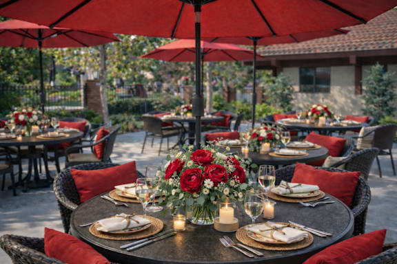 Outdoor patio dining with red umbrellas and table settings at Roseville Commons Senior Living Apartments, Roseville, California