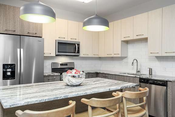 A modern kitchen with a marble countertop and wooden chairs.