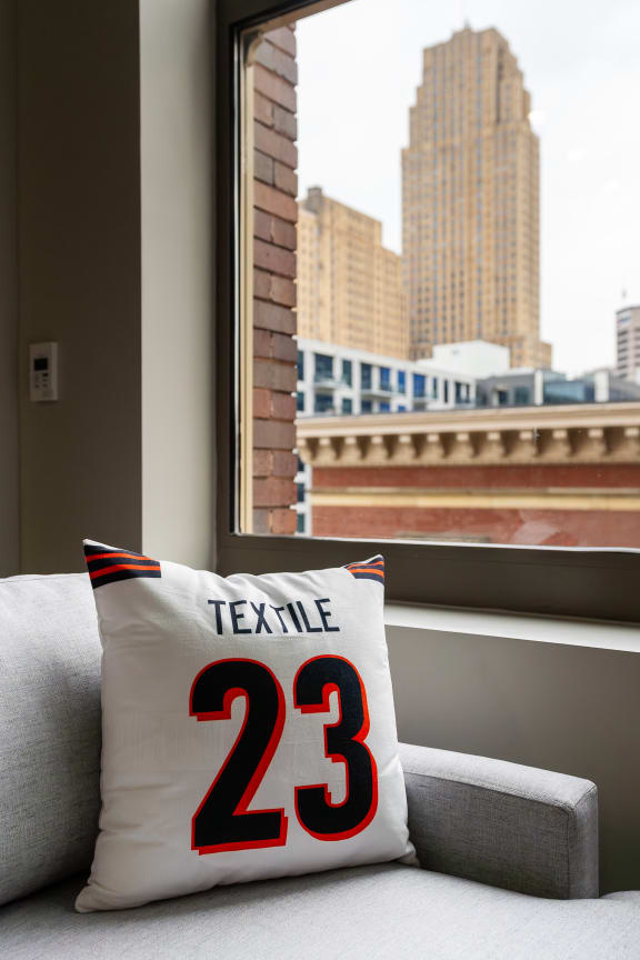 A pillow with the number 23 on it sits on a couch in front of a window. at Textile Apartments, Cincinnati, OH, 21286