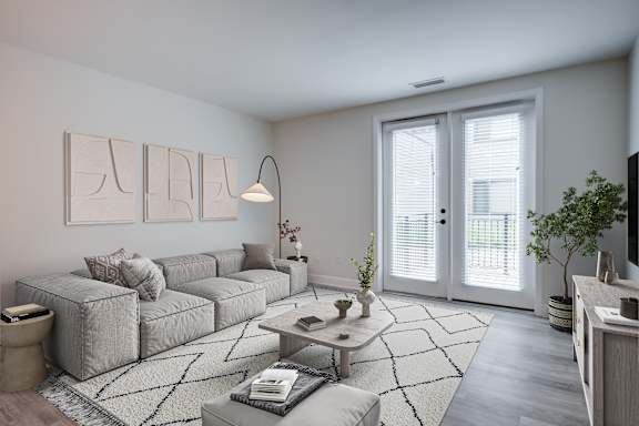 A modern living room with a grey sofa, a coffee table, and a large window with blinds. at The MK, Indiana