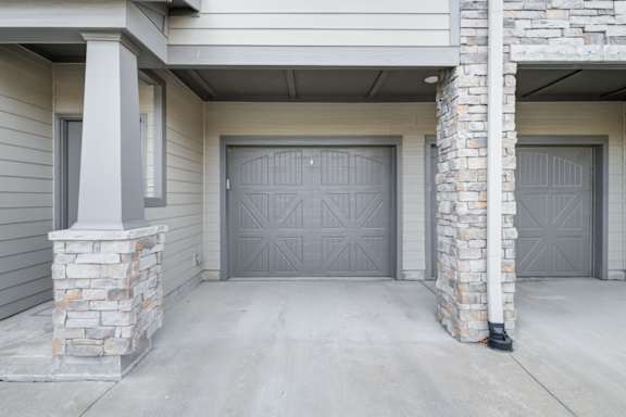 A house with a grey garage door and stone pillars.