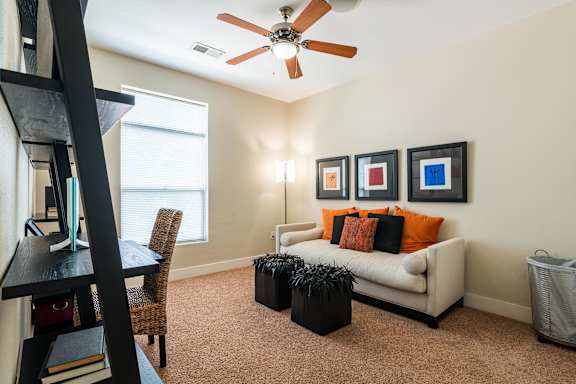 A living room with a white couch, a black ottoman, a ceiling fan, and three framed pictures on the wall. at CityView, North Kansas City, 64116