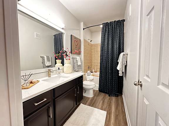 A bathroom with a white sink, black cabinets, and a white toilet at Grand Villas Apartments, Katy